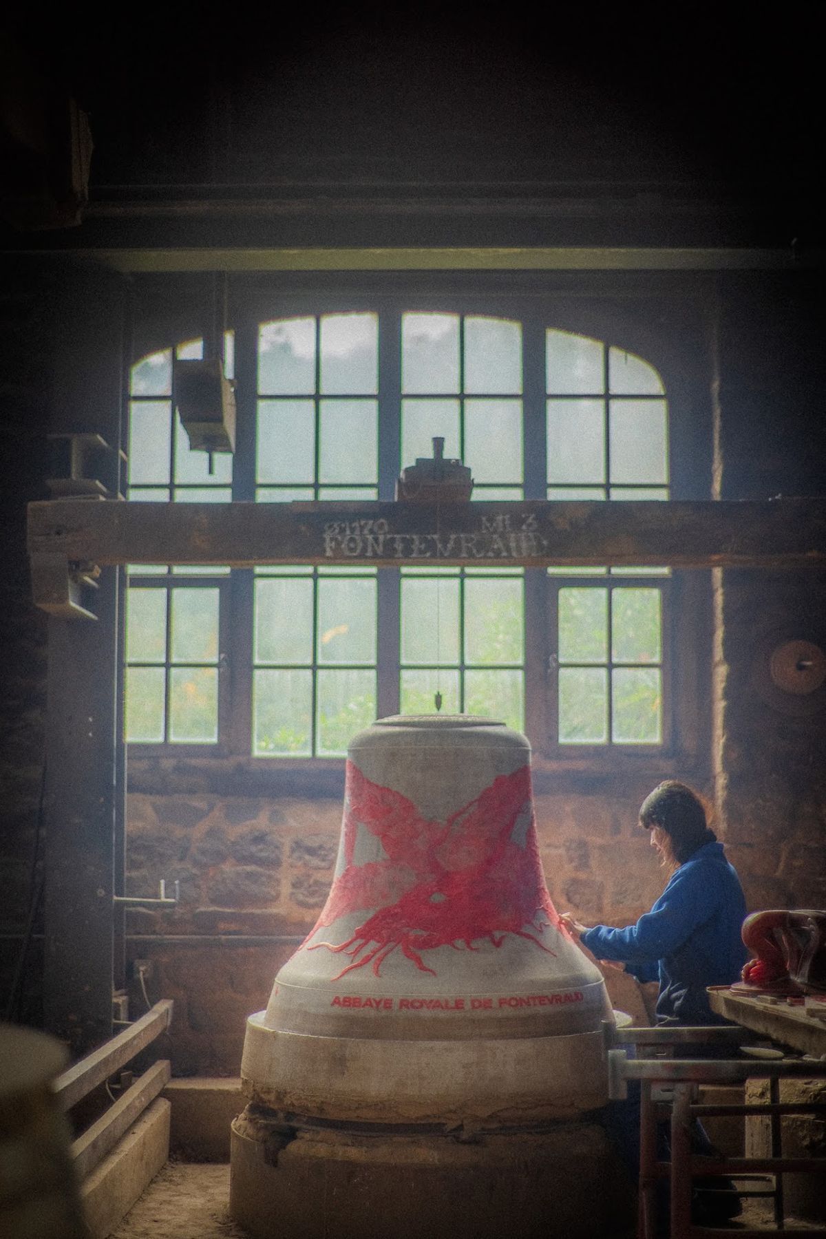 Une artiste peint une cloche dans l’atelier de la fonderie, devant une grande verrière